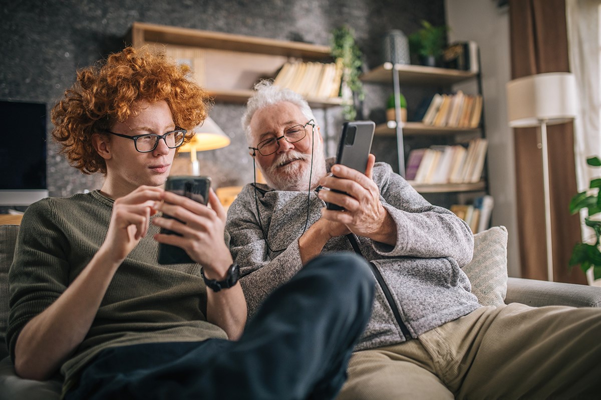 Ung kille och äldre man sitter med sina mobiltelefoner